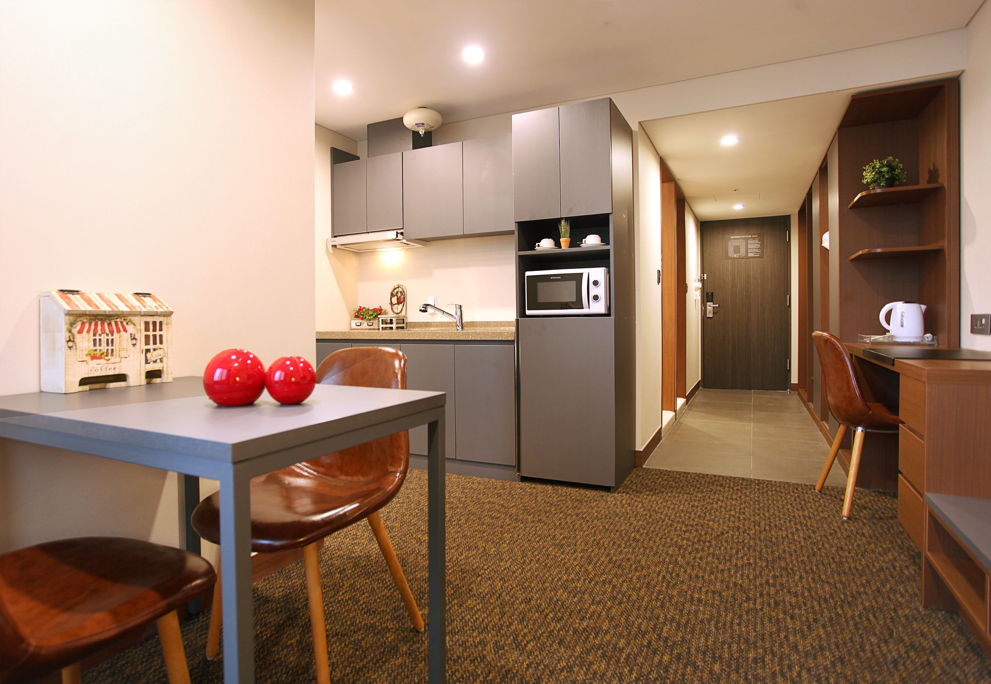 A compact kitchen with grey cabinets, a microwave, and a coffee machine. There is a small dining area with a table and two chairs.