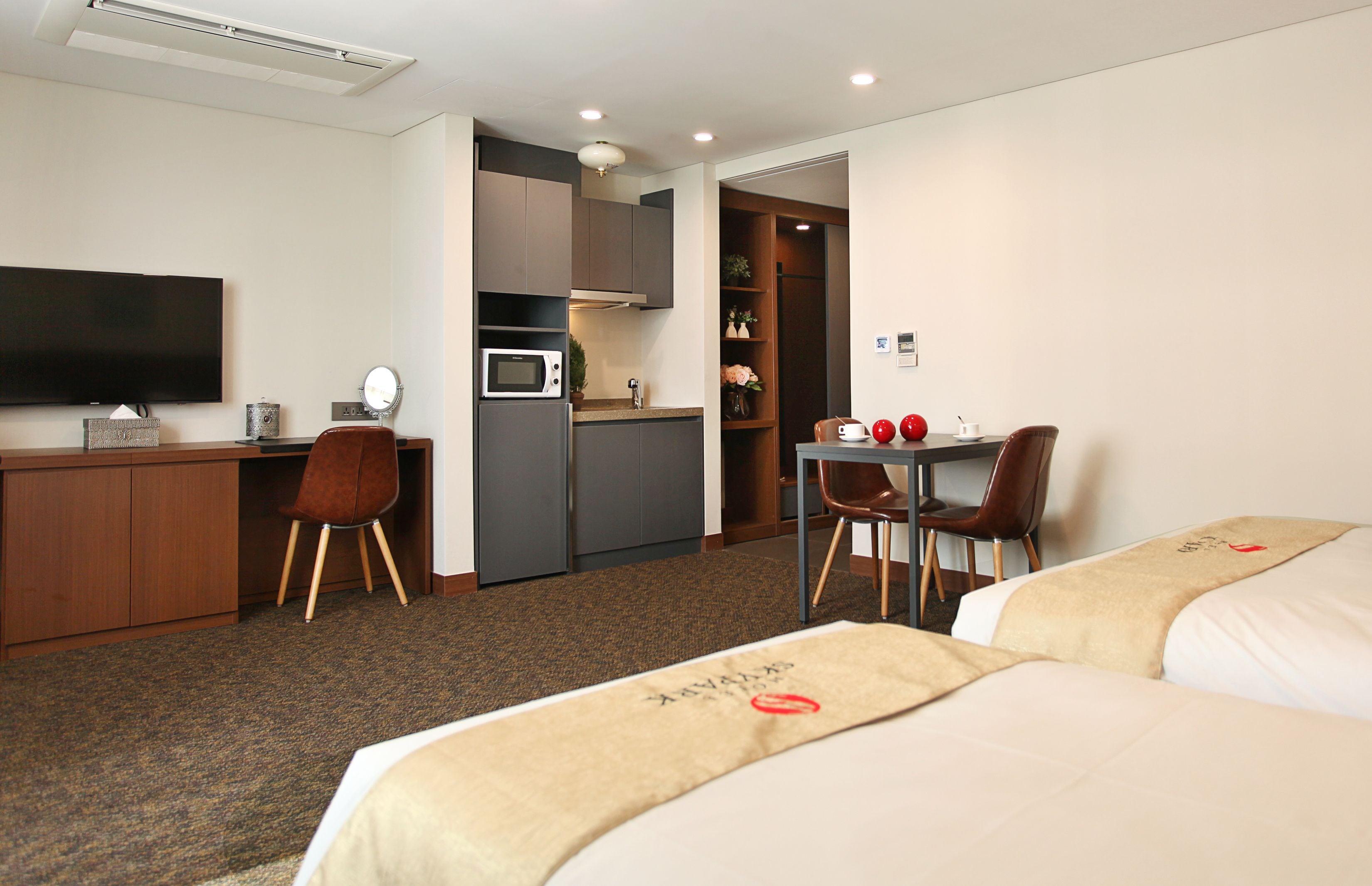 A hotel room with a bed, a desk, a chair, a TV, a microwave, and a small kitchenette.
