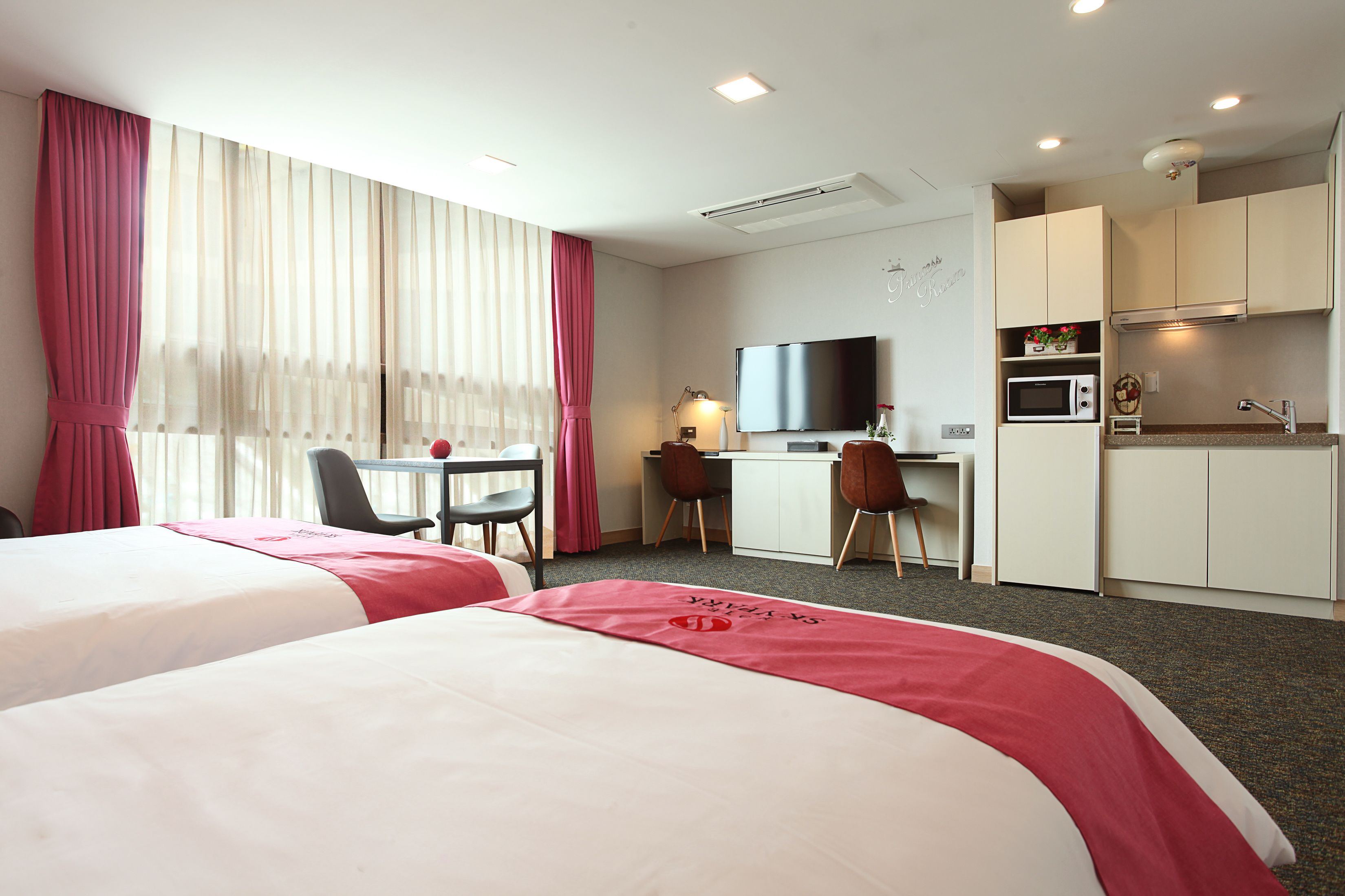 Habitación de hotel con dos camas, un escritorio con silla, televisor, microondas y kitchenette.