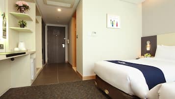 A hotel room with a bed, a nightstand, a wall-mounted clock, and a door with an emergency exit plan.