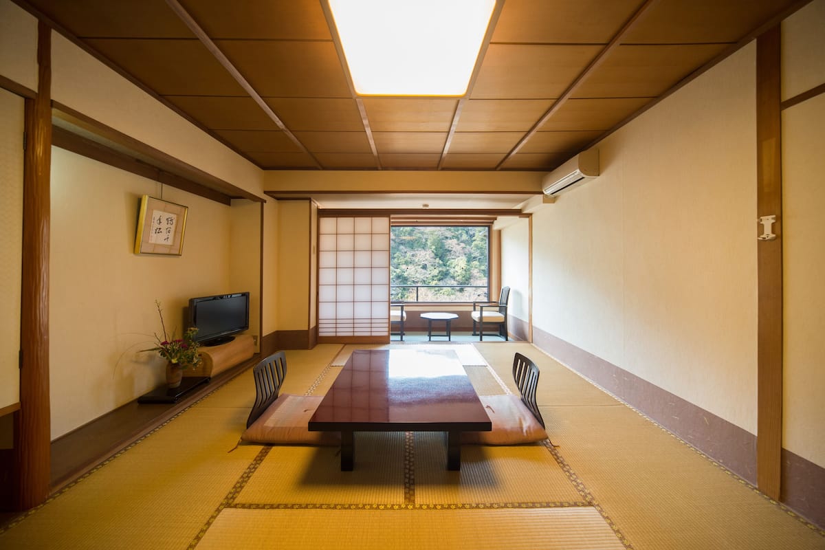 Ett traditionellt japanskt rum med tatamimattor på golvet, ett lågt bord och en tv som står på ett stativ.