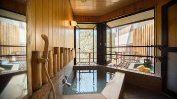 Uma onsen japonesa tradicional com interiores de madeira, um banho de águas termais e vista para a floresta circundante.