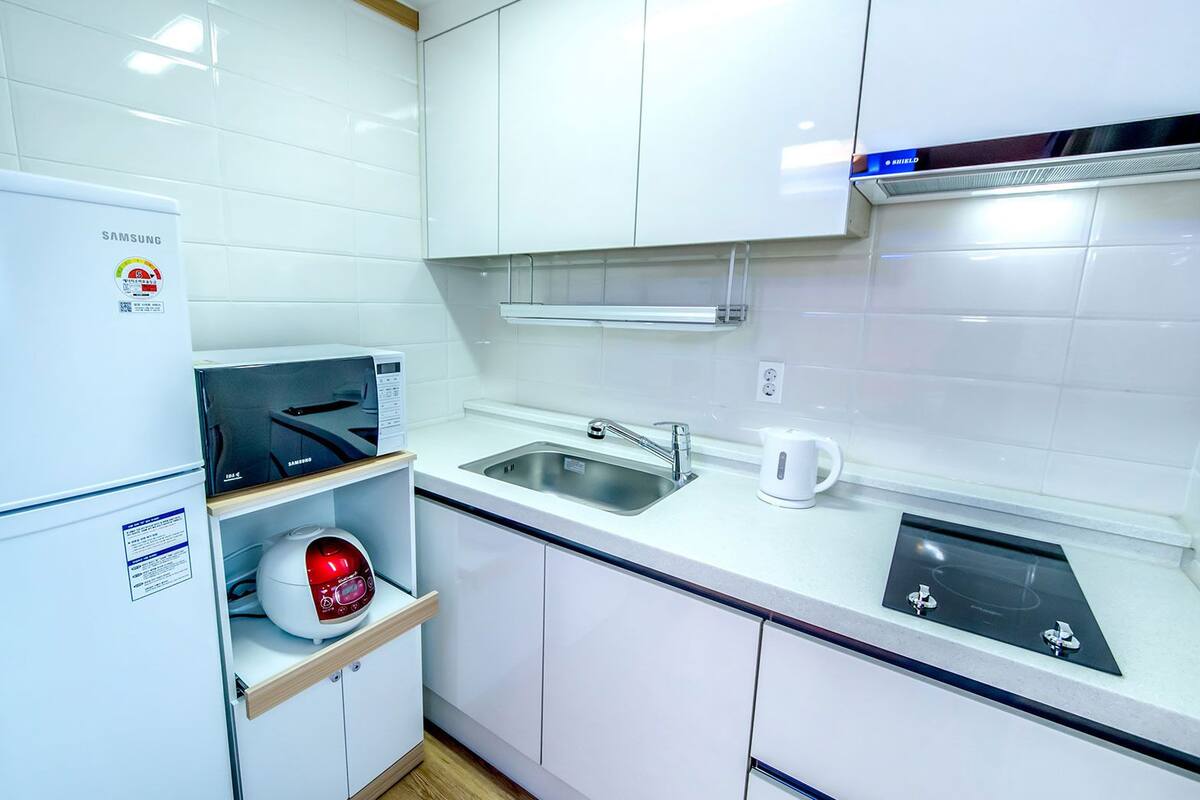 Una cocina moderna con armarios blancos, microondas integrado, hervidor y pileta.