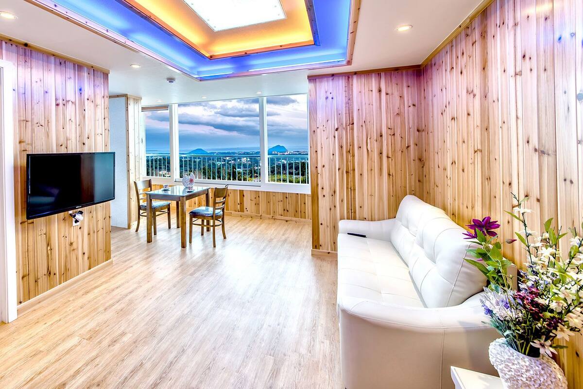 Una sala de estar moderna con televisor, paredes de madera, un sofá y un comedor con vistas.