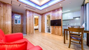 Ett modernt hotellrum med träpanel på väggarna, en röd soffa, ett träbord med en stol, en tv och ett köksutrymme med en diskho och skåp.