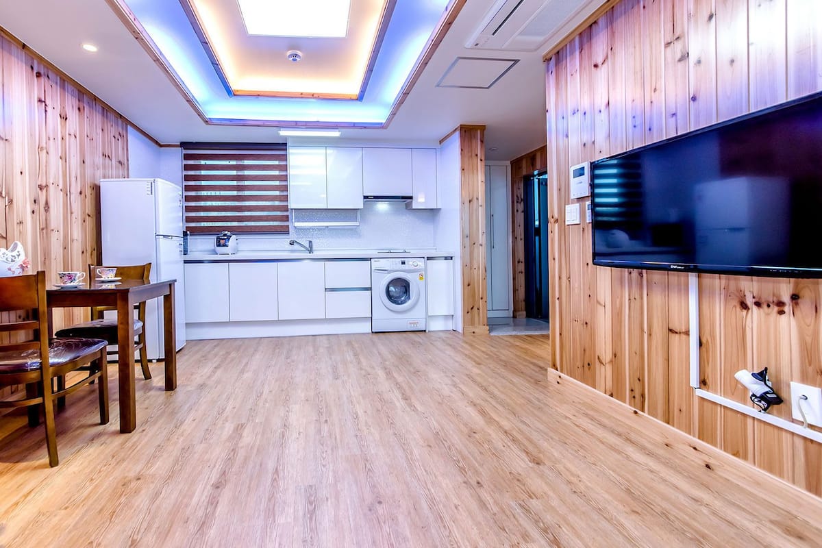 Un espacio habitable compacto con kitchenette, comedor y televisor montado en la pared.