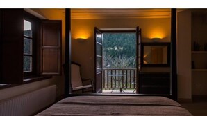 A bedroom with a large bed, a chair, a TV, and a balcony with a view of trees. - Epoches Luxury Suites (Karpenisi)