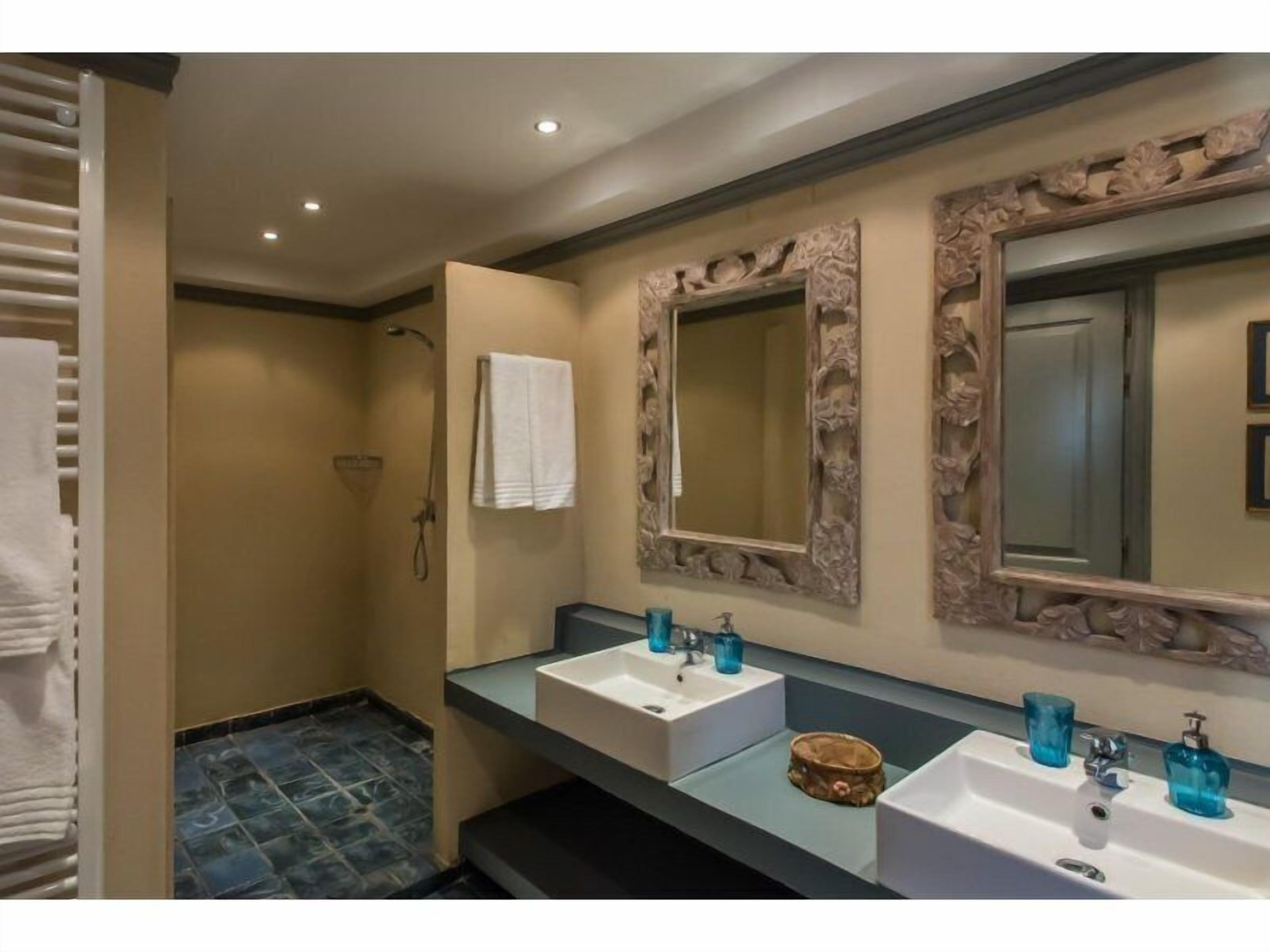 Un baño con dos lavamanos, ducha y un espejo grande con marcos ornamentados.