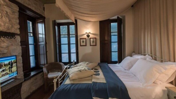 A bedroom with a bed, a television, a chair, and a window with curtains. - Epoches Luxury Suites (Karpenisi)