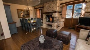 A cozy living room with a stone fireplace, wooden flooring, and comfortable seating. - Epoches Luxury Suites (Karpenisi)