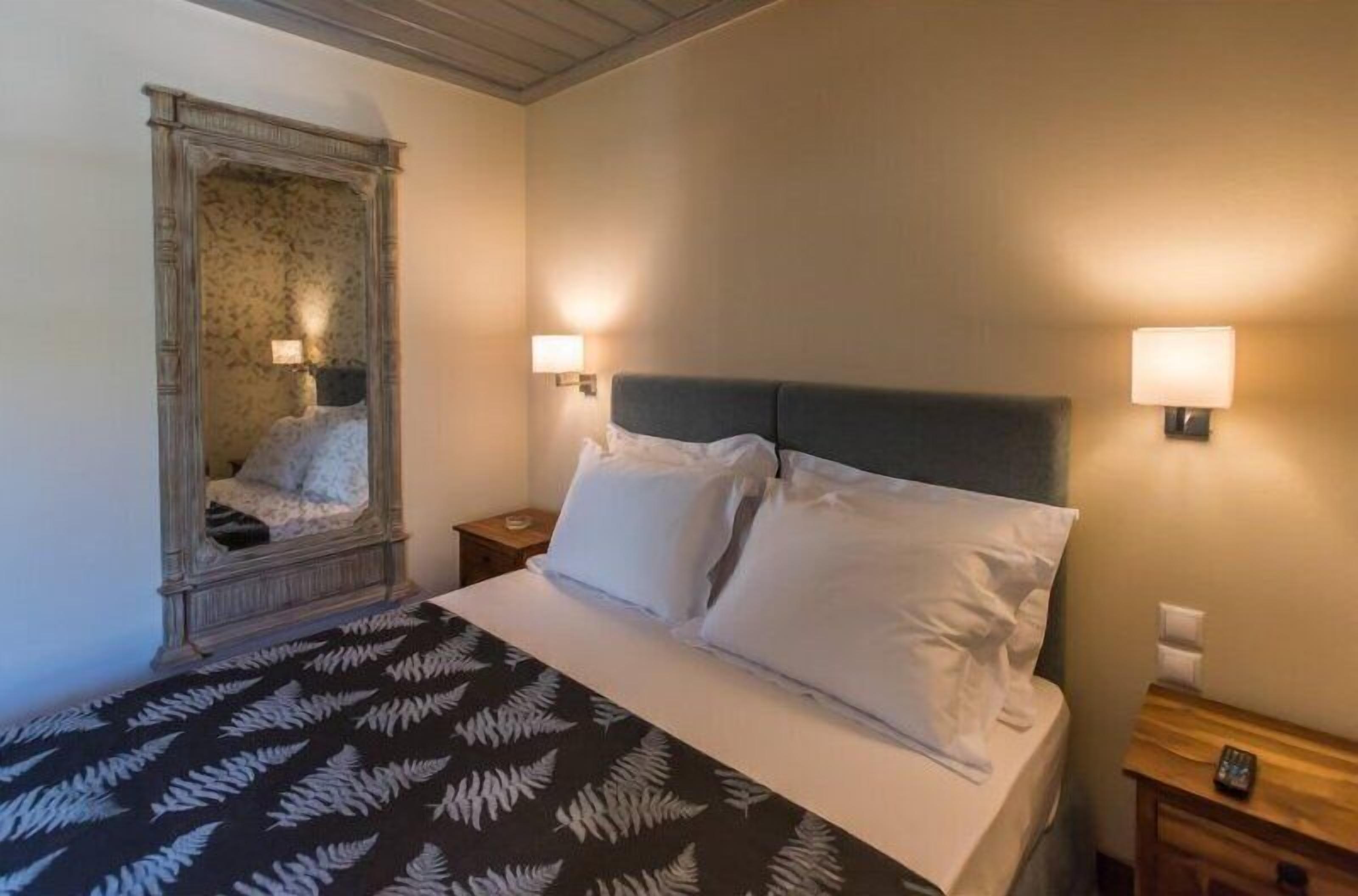 Una habitación de hotel con cama, mesita de noche, espejo e iluminación en la pared.