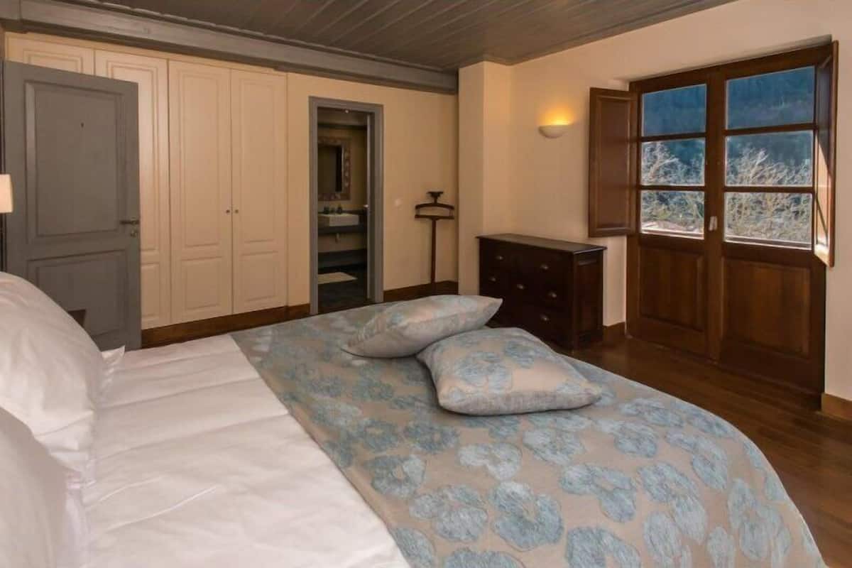 Un dormitorio con cama, armario, cómoda y ventana con vista a árboles.