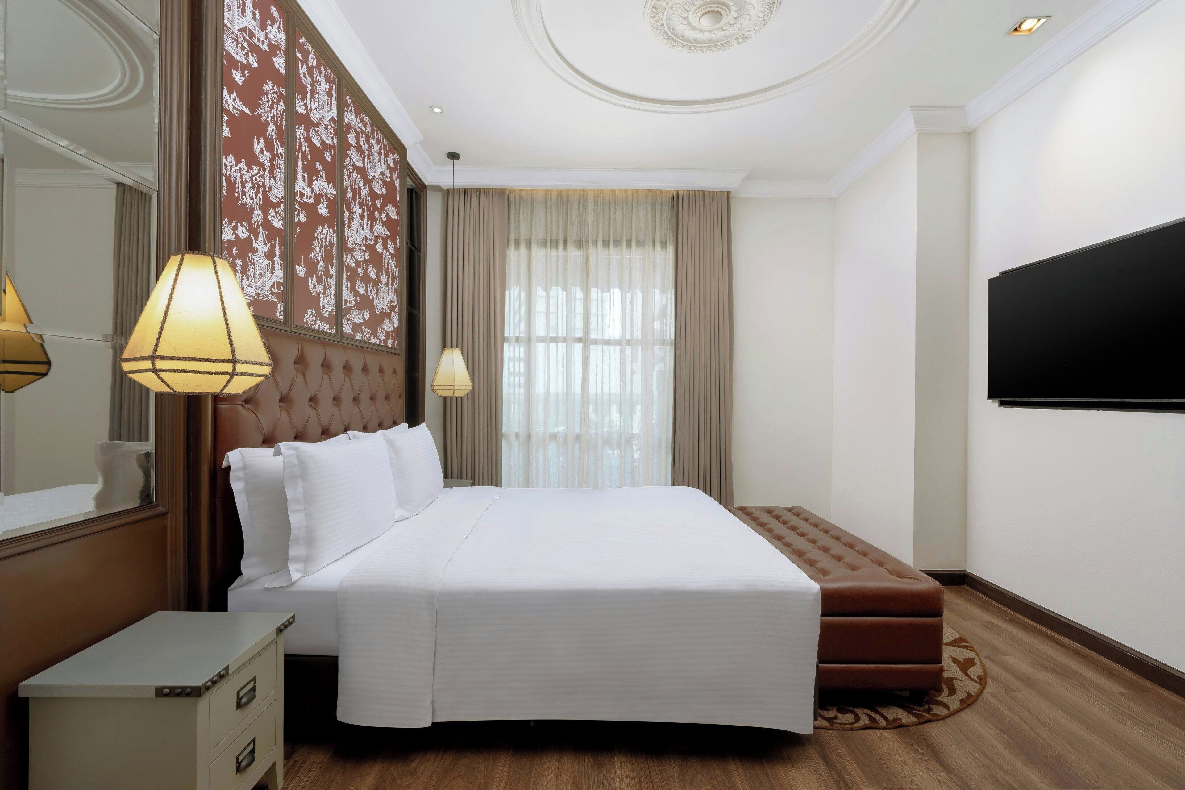 A hotel room with a large bed, a flat-screen TV, a nightstand, and a decorative wall panel.