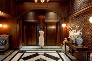 A woman standing in front of a wooden double door with a patterned wall and a marble floor. - Metropole, Bangkok, a Tribute Portfolio Hotel (Bangkok)