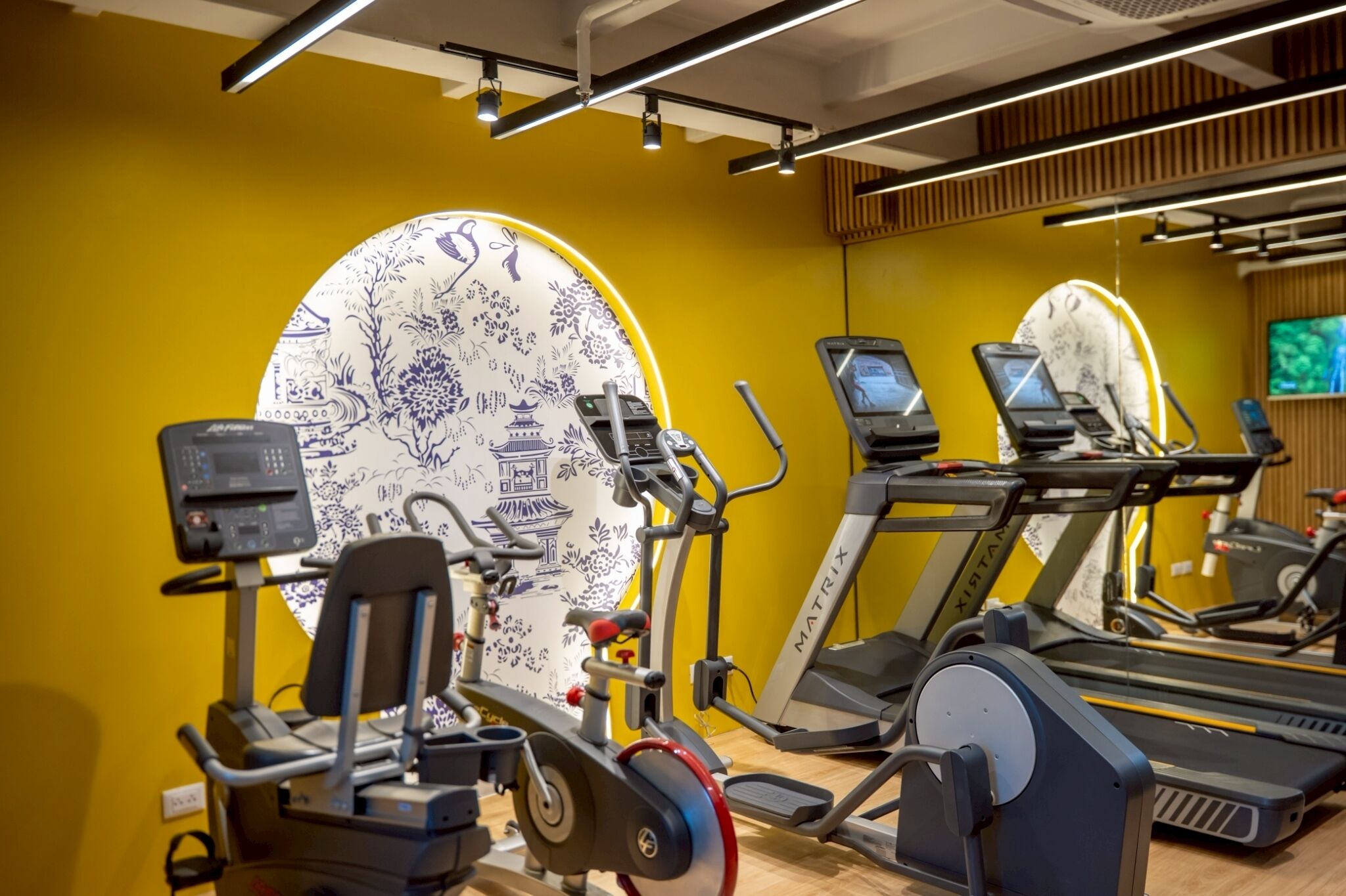 Un gimnasio con equipo de ejercicio, un espejo decorativo grande y un televisor en la pared.