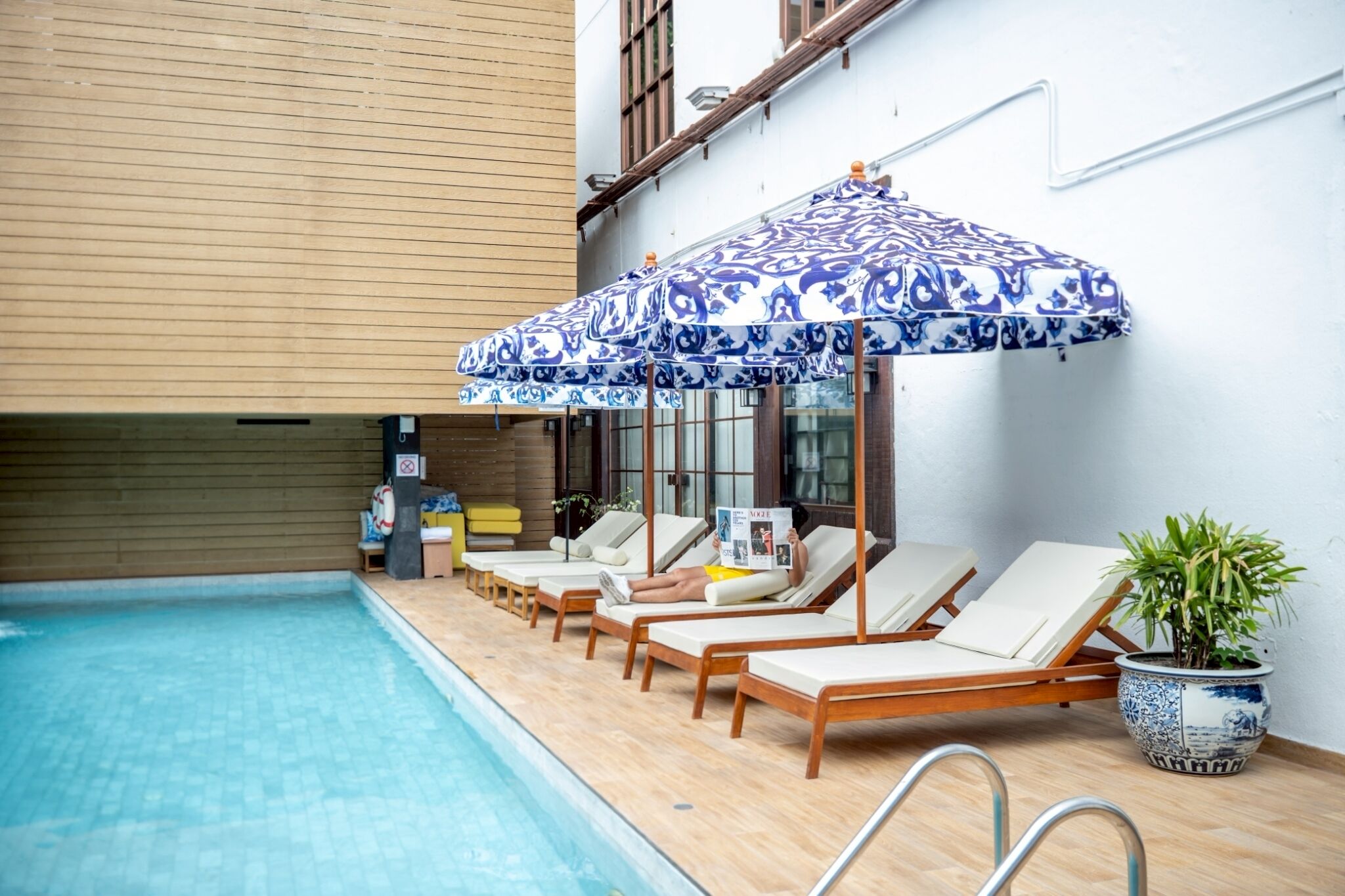 A poolside area with lounge chairs and umbrellas, a potted plant, and a wooden wall.
