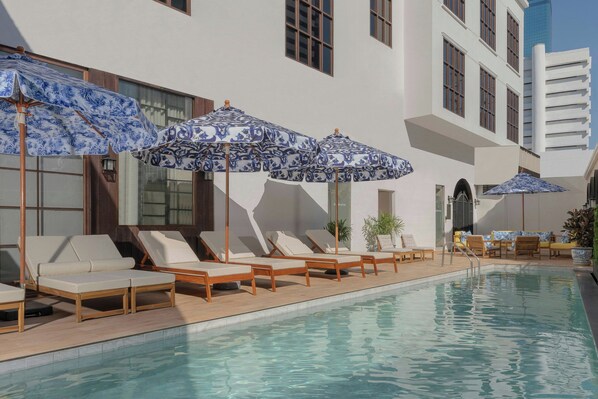 A poolside area with lounge chairs and umbrellas, a clear pool, and a building with large windows and balconies. - Metropole, Bangkok, a Tribute Portfolio Hotel (Bangkok)