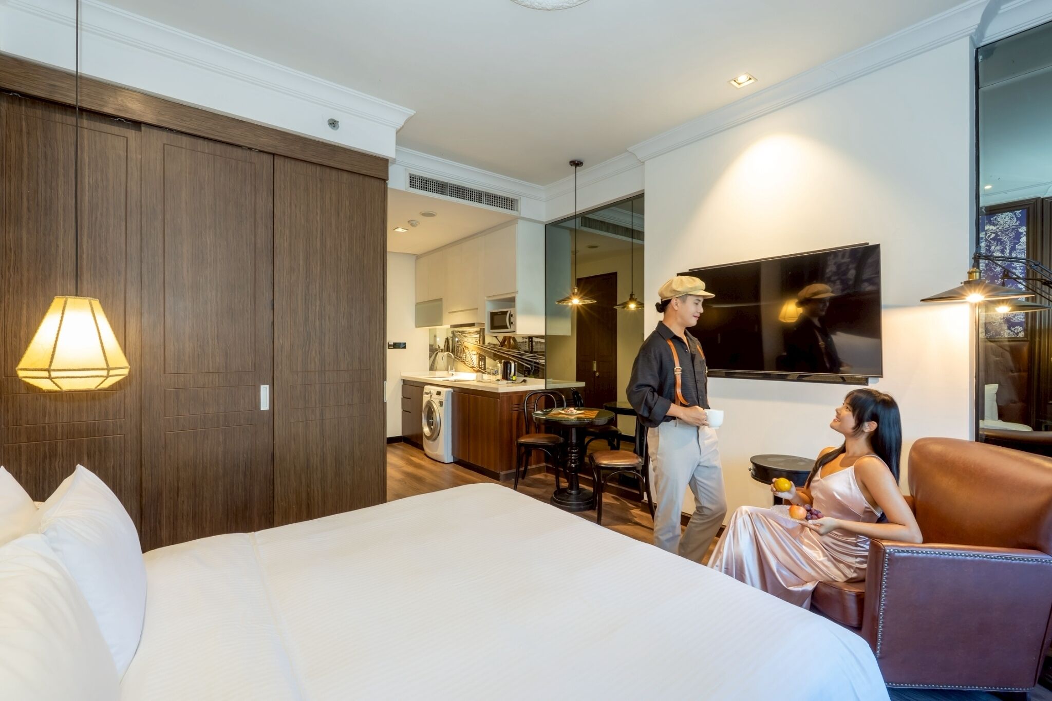 Ein Hotelzimmer mit einem großen Bett, einer Sitzecke mit Tisch und Stühlen, einer Küchenzeile und einem großen Spiegel.