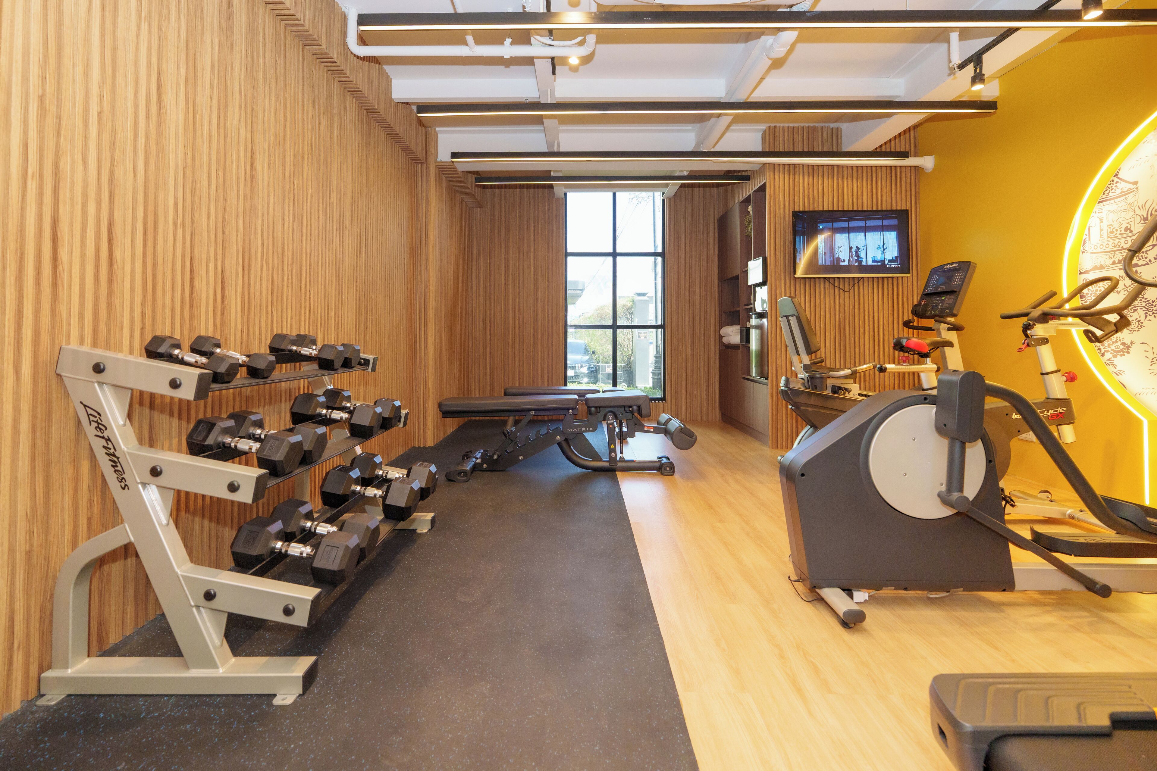 Une salle de sport équipée d’un tapis de course, d’un vélo elliptique et d’haltères.