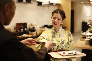 A person in traditional attire serving food to another individual. - Yoshidaya Sannokaku (Kaga)