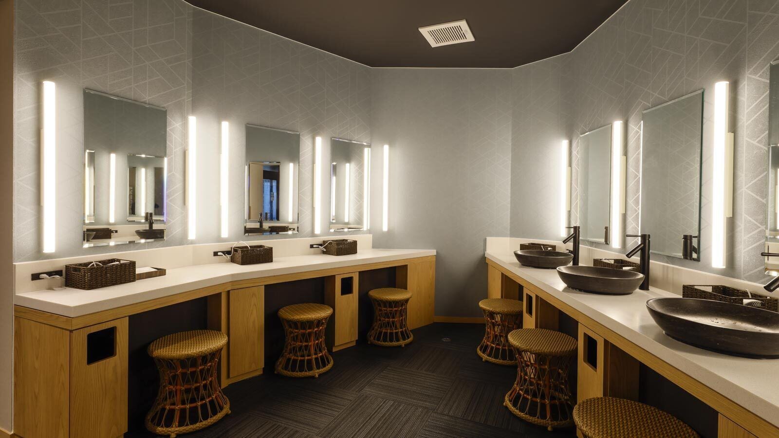 Un baño moderno con varios lavamanos, espejos y taburetes de mimbre.