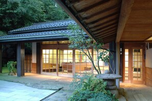 A traditional Japanese building with a tiled roof, large glass doors, and a stone lantern. - Yoshidaya Sannokaku (Kaga)