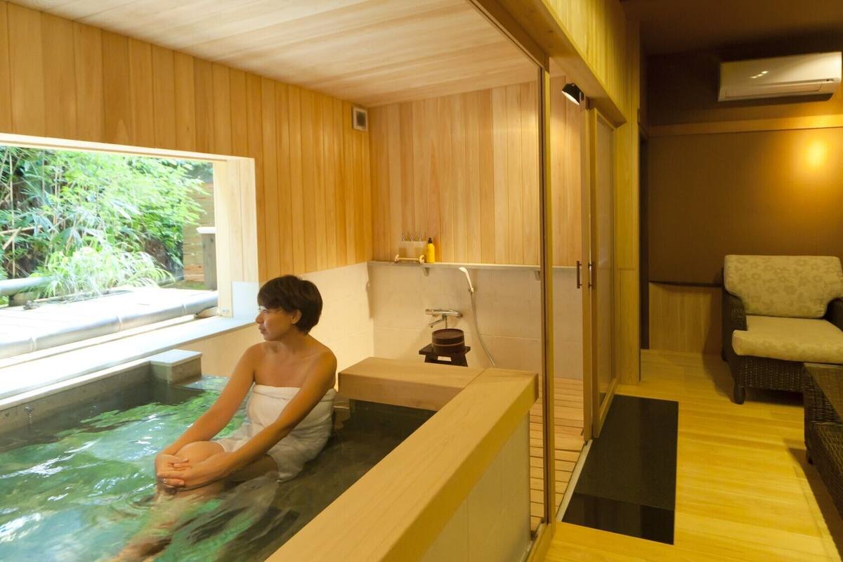 Un cuarto de spa con una bañera, una silla y una ventana con vistas a zonas verdes.
