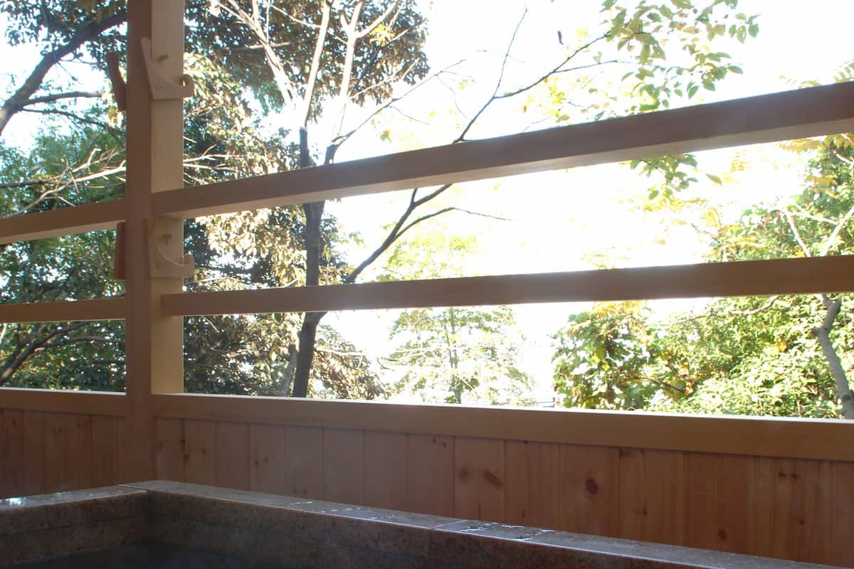 Un spa de madera con bañera de hidromasaje, vigas de madera y vistas a árboles a través de amplios ventanales.