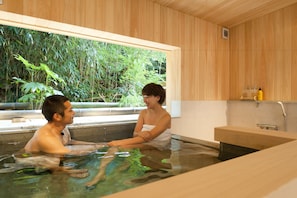 Una pareja en una habitación con paneles de madera y un ventanal grande con vistas a un jardín exuberante.