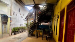 A narrow alleyway with a staircase leading to a building with a red door. There are potted plants along the left side and a small table with chairs in the center. - Amelia 2 Guest House (Medan)