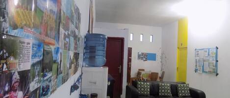 A living room with a couch, a water dispenser, a bulletin board, and a door.