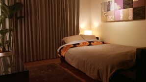 A neatly made bed with a floral bedspread, a bedside lamp, and a potted plant in a corner. - Chelsea24 Kyoto (Kyoto)