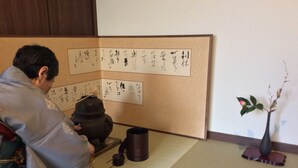 A traditional Japanese room with tatami flooring, a shoji screen with calligraphy, a tea ceremony setup, and a bonsai tree. - Chelsea24 Kyoto (Kyoto)
