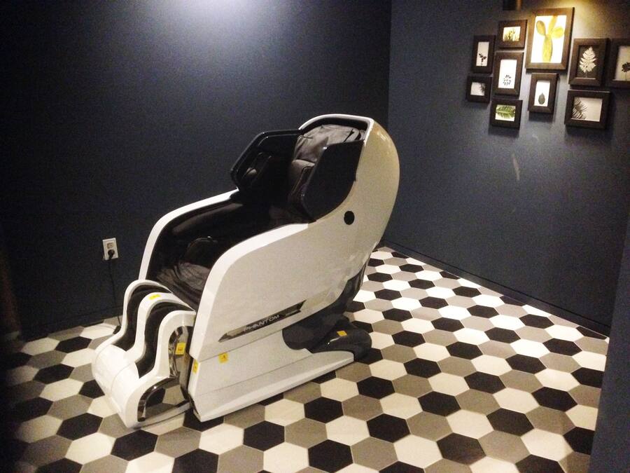 A room with a hexagonal patterned floor, a massage chair, and framed botanical prints on the wall.