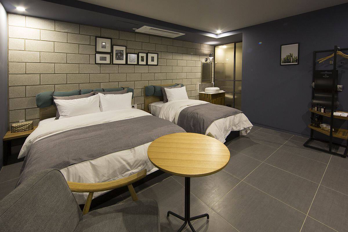 A modern hotel room with two beds, a round wooden table, and a brick-patterned wall.