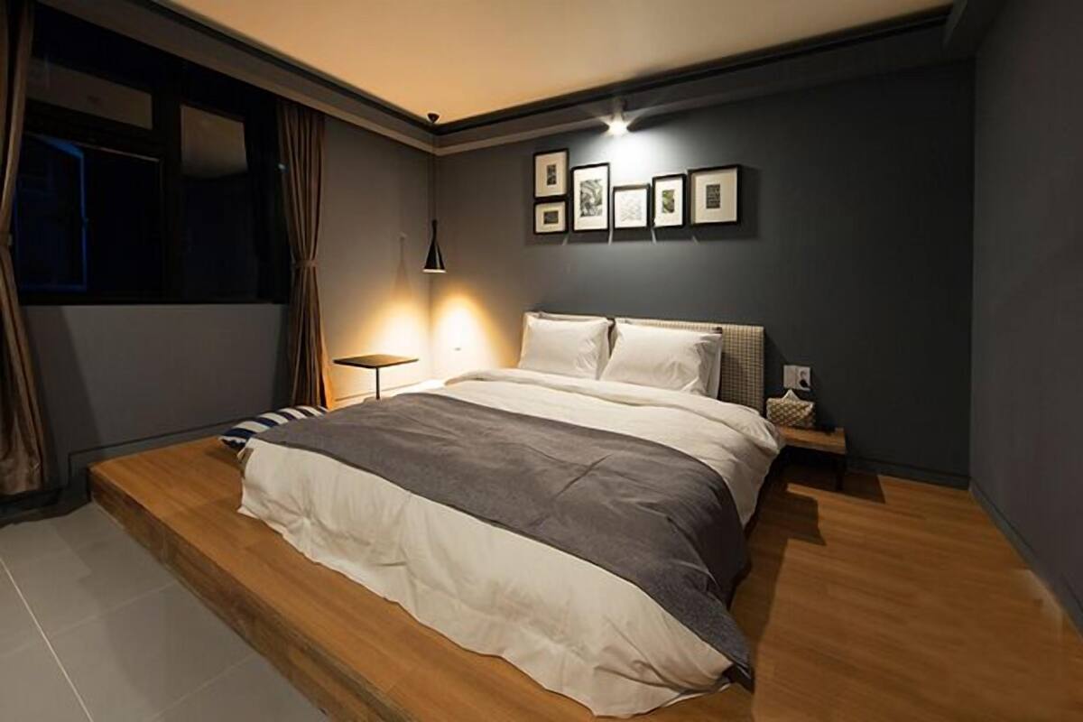 A bedroom with a bed, bedside tables, a nightstand, a lamp, and framed pictures on the wall.