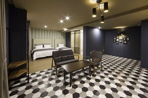 A hotel room with a large bed, a sofa, a table, and a chair. The room has a checkered floor and a dark blue wall with framed pictures. - Gimhae Brown Dot Hotel Waterpark (Gimhae)