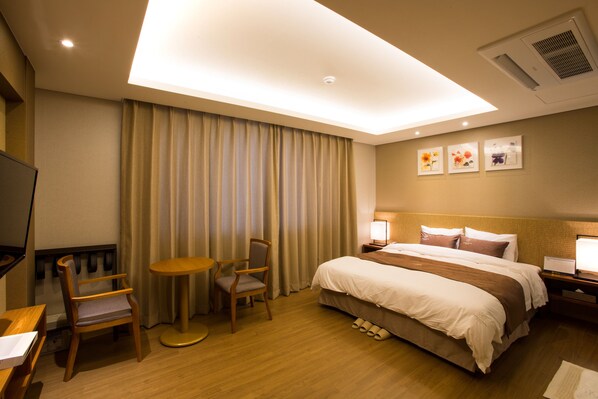 Ein Hotelzimmer mit Bett, Schreibtisch, Stuhl, kleinem Tisch und einem Fenster mit Vorhängen.