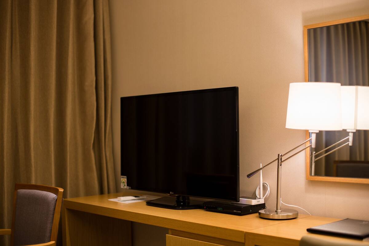 Un escritorio de hotel con un televisor de pantalla plana, una lámpara y una computadora portátil.