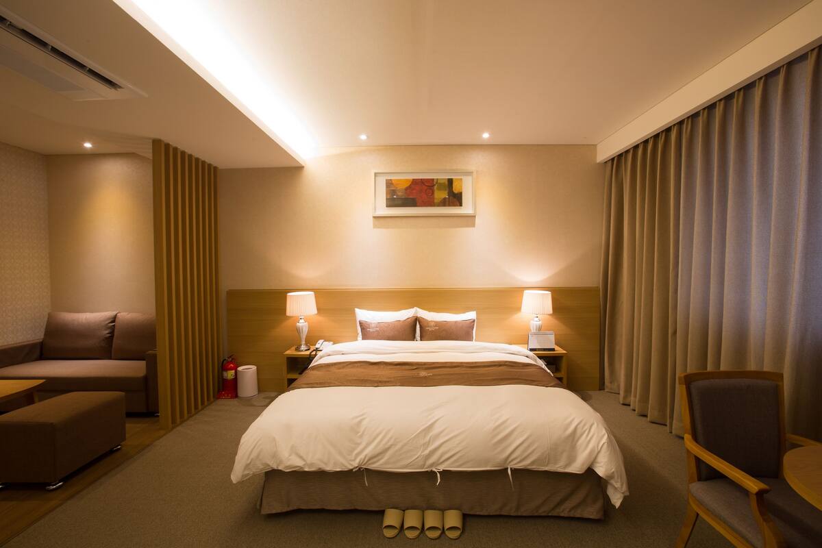 Una habitación de hotel con una cama grande, dos mesitas de noche, una silla, un sofá y un cuadro en la pared.