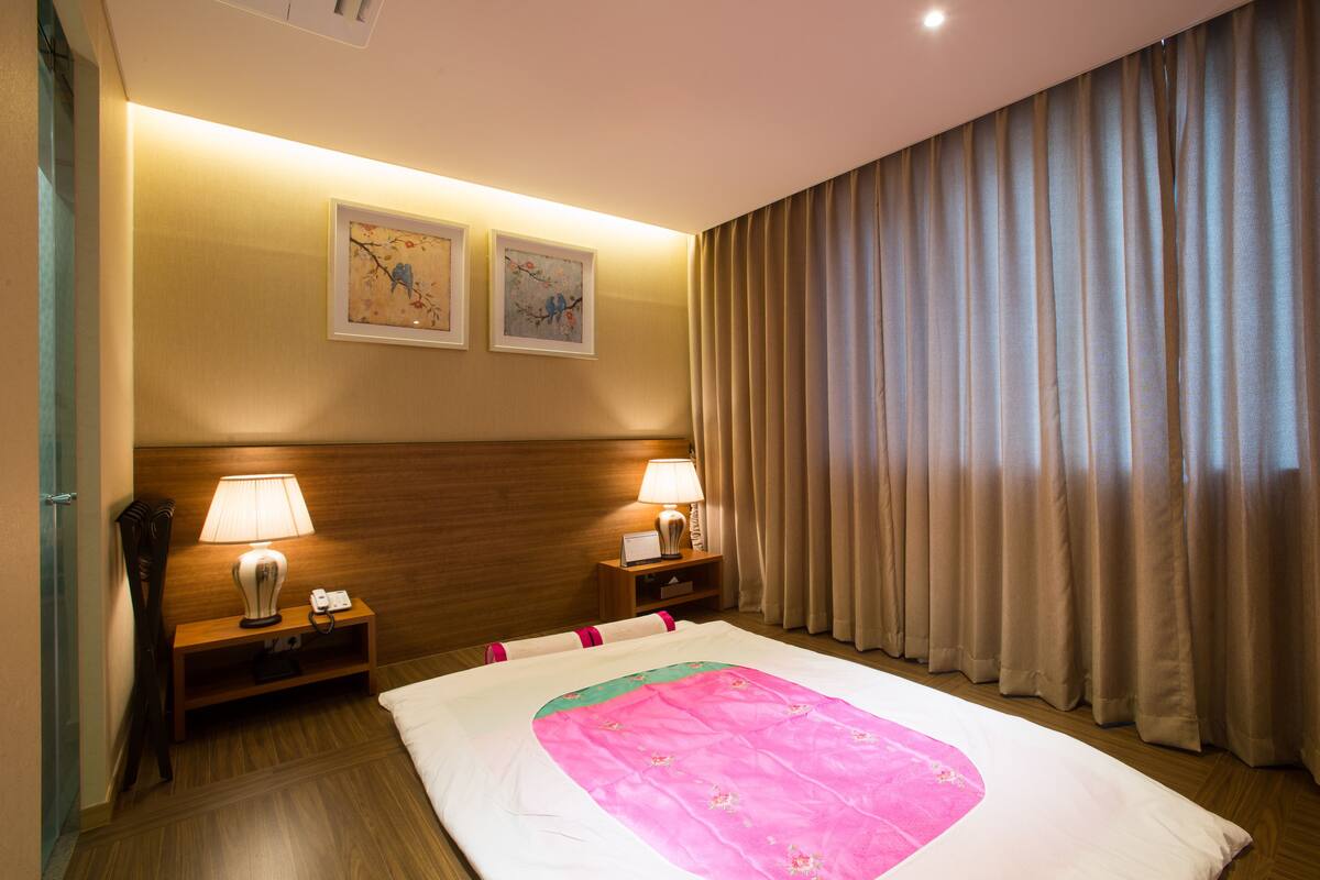 Habitación de hotel con una cama grande, dos lámparas de noche, un cabecero de madera y dos cuadros en la pared.