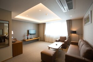 Ein modernes Hotelzimmer mit einer Couch, einem Couchtisch, einem Fernseher und einem Schreibtisch.