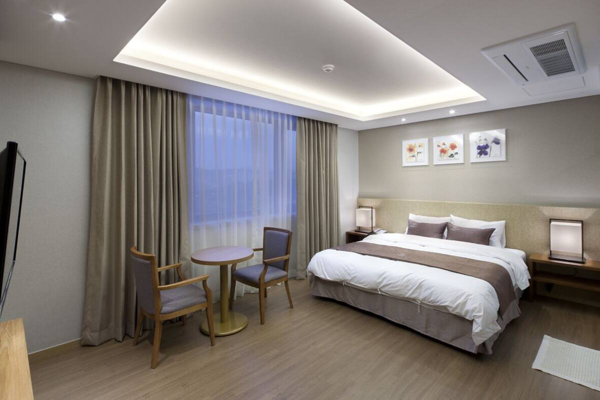 Habitación de hotel con cama, mesitas de noche, escritorio con sillas, ventana con cortinas y decoración en la pared.