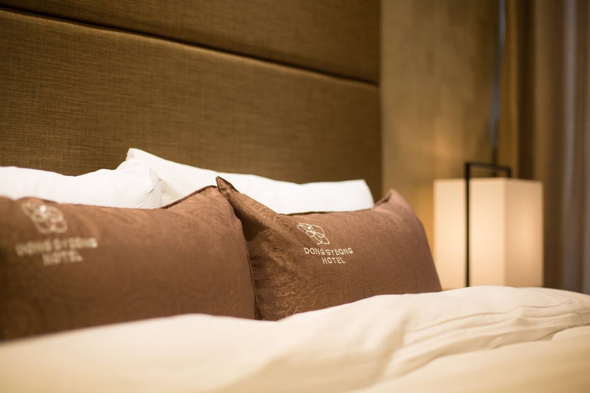 Una cama con ropa de cama blanca y almohadas marrones, con el logo del Dong Shing Hotel.