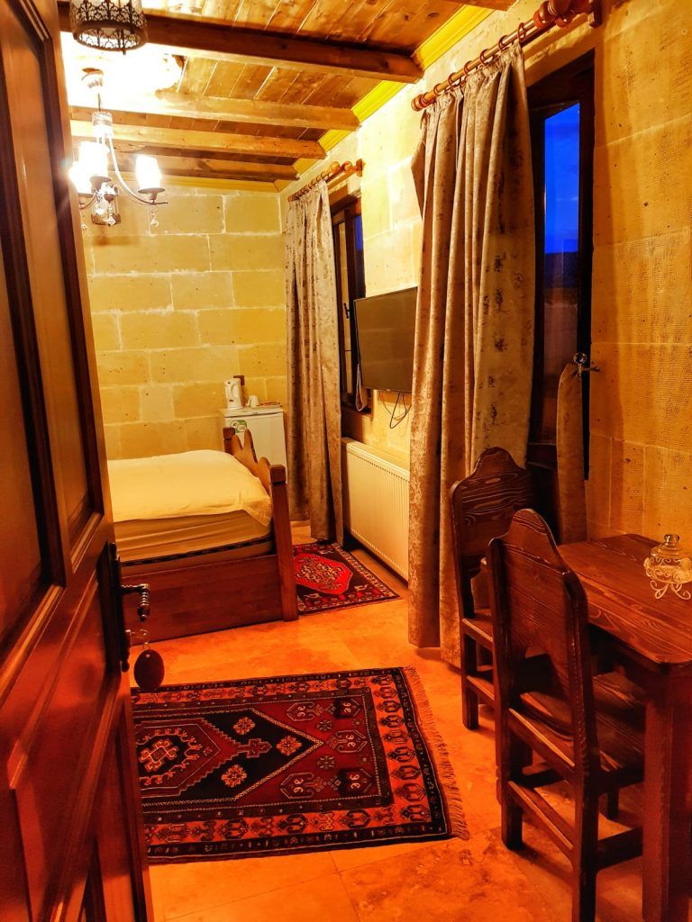 A narrow room with a bed, a table, and chairs, a radiator, and a television.