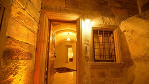 Un étroit couloir en pierre, avec une porte en bois et une fenêtre grillagée.