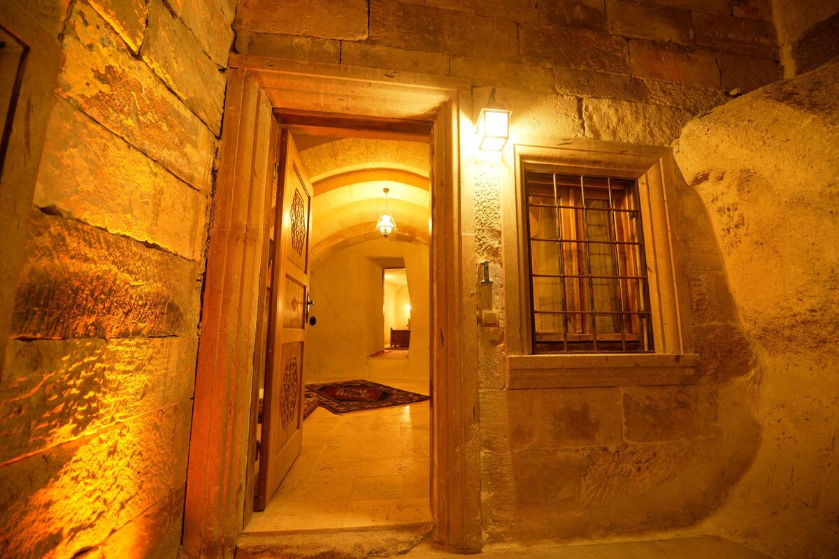 Un estrecho pasillo de piedra con una puerta de madera y una ventana con barrotes.