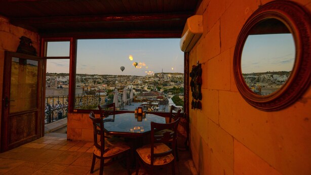 Un coin repas avec une table et des chaises, une vue sur un paysage urbain avec des montgolfières, et un miroir rond accroché au mur.
