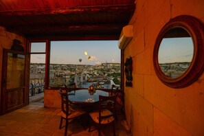 A dining area with a table and chairs, a view of a cityscape with hot air balloons, and a round mirror on the wall. - Vineyard Cave Hotel (Nevsehir)