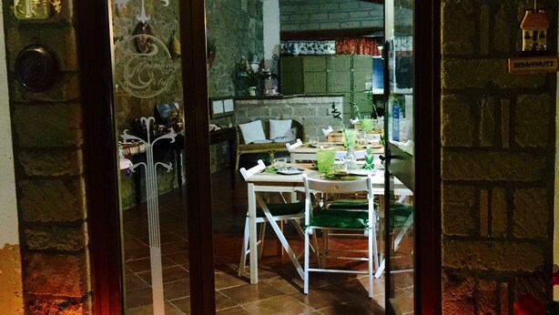An open door leading to a dining area with a table and chairs, a brick wall, and a sign that reads "BENVENUTI". - B&B Maremma Nel Tufo (Pitigliano)